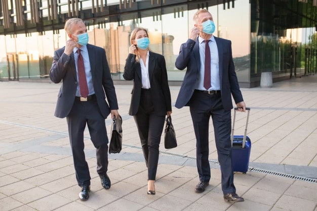 three business people wearing masks walking down a sidewalk.