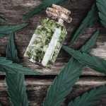 a glass jar filled with marijuana leaves on top of a wooden table.