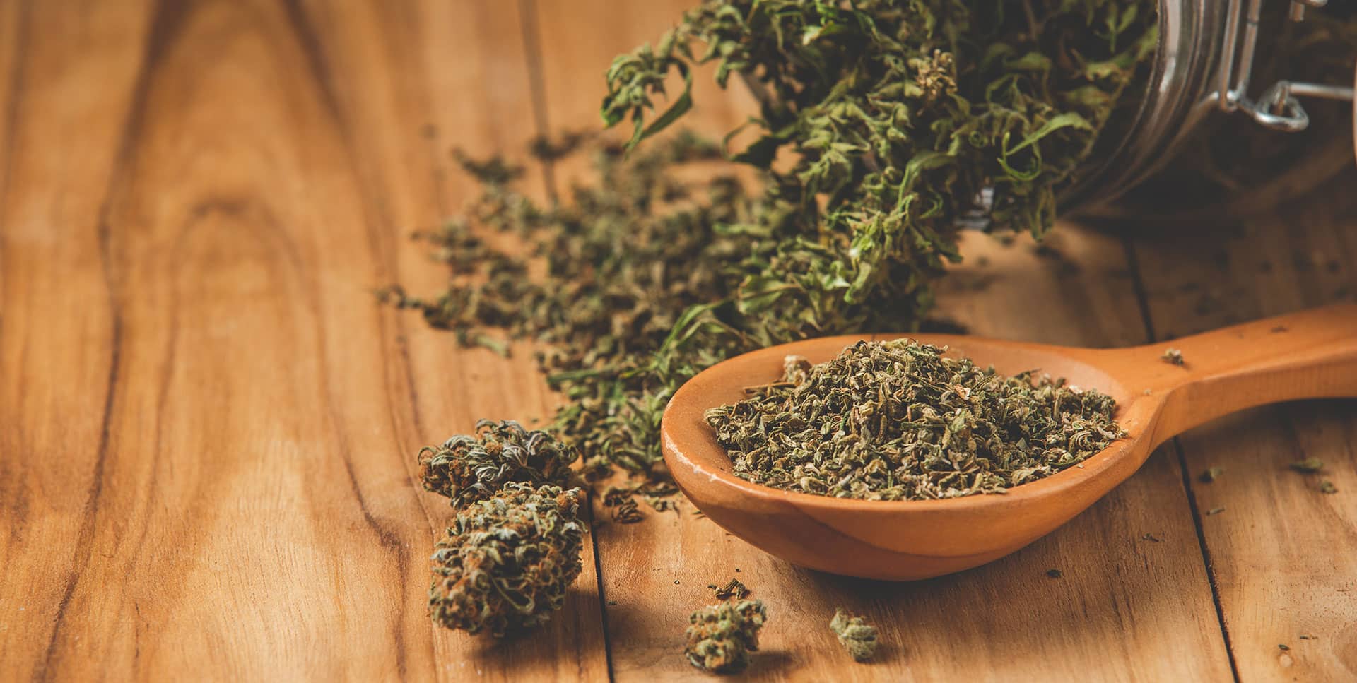 a wooden spoon filled with dried herbs on top of a wooden table.